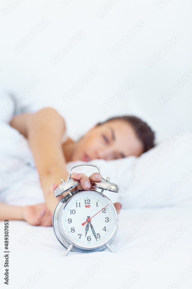 5 more minutes.... Shot of a sleepy young woman reaching out to turn off her alarm clock.