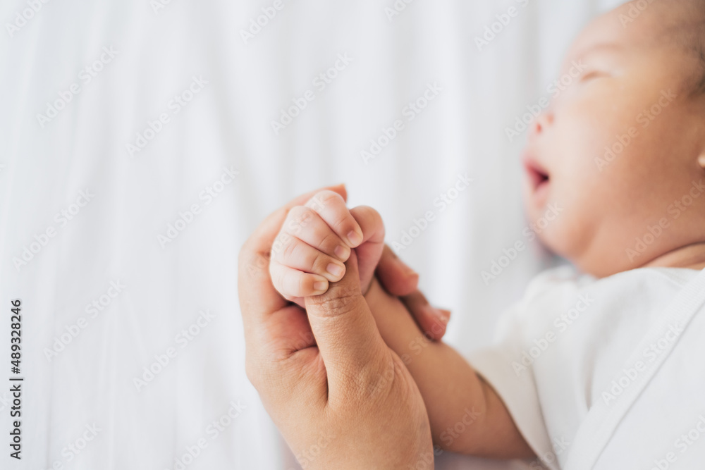 Mother touch her newborn baby hand gently on white bed