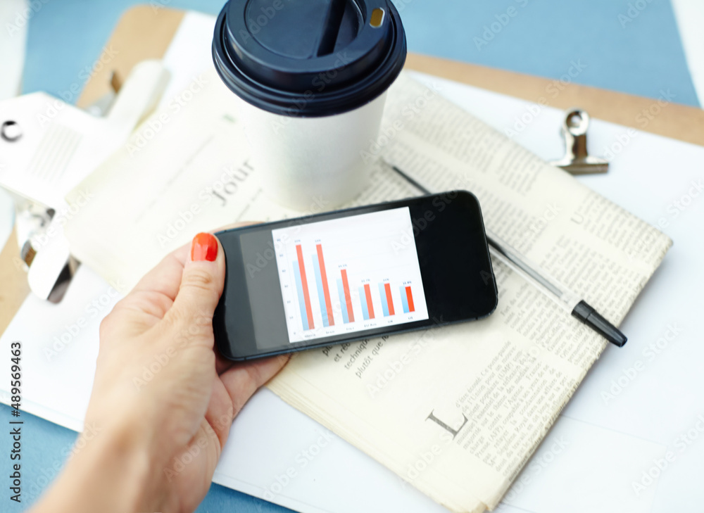 One last look at the numbers. Hand holding smartphone with bar chart on screen with disposable cup, 