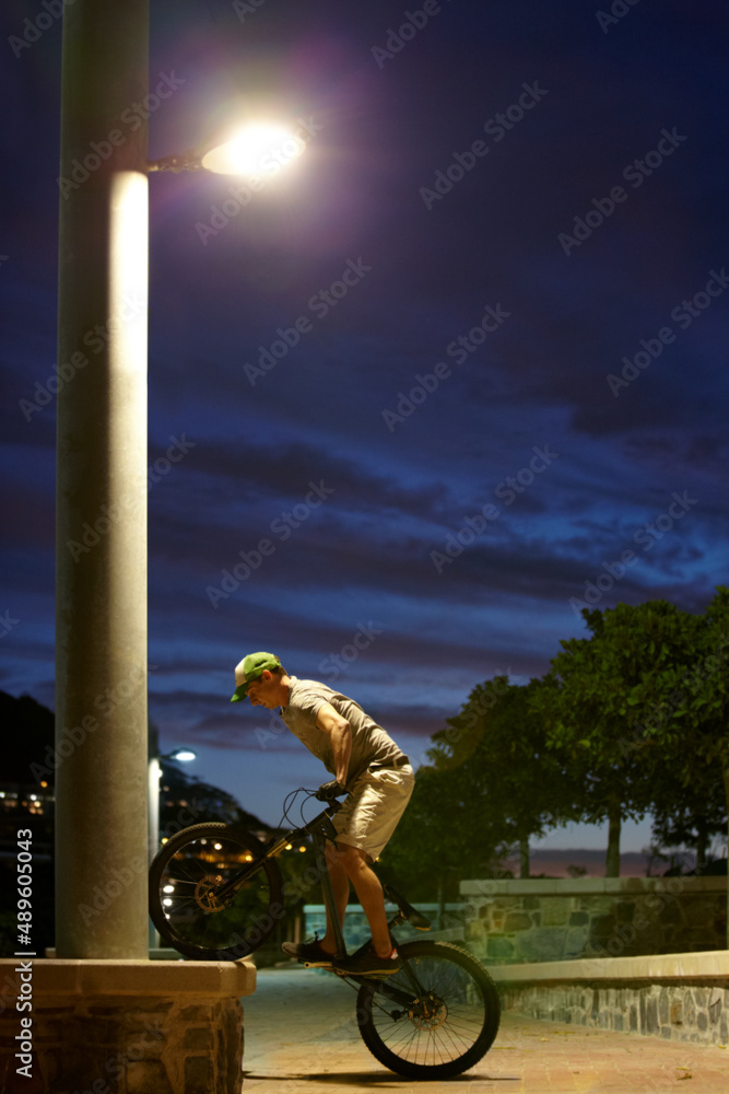 永远不要睡觉，只需骑行。一名男子晚上在路灯下骑自行车玩把戏的镜头。