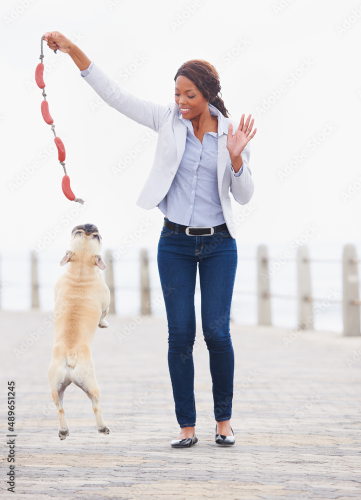 跳得更高。一个美丽的非洲女人在海滨大道上和她的狗玩耍。