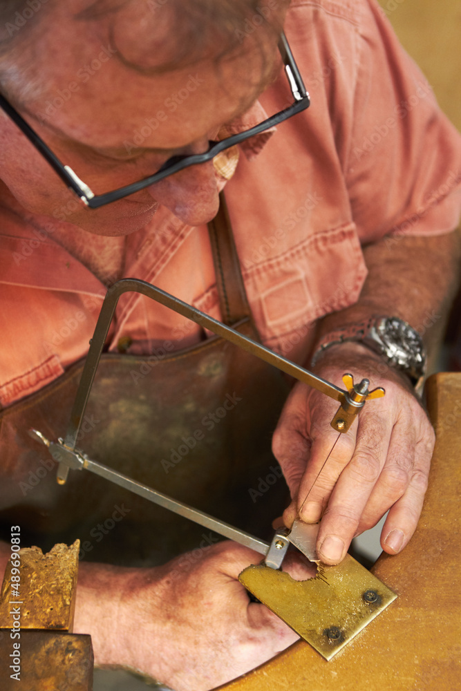 Carefully cutting out the shape - Jewelry manufacturing. Top view of a goldsmith about to saw into a