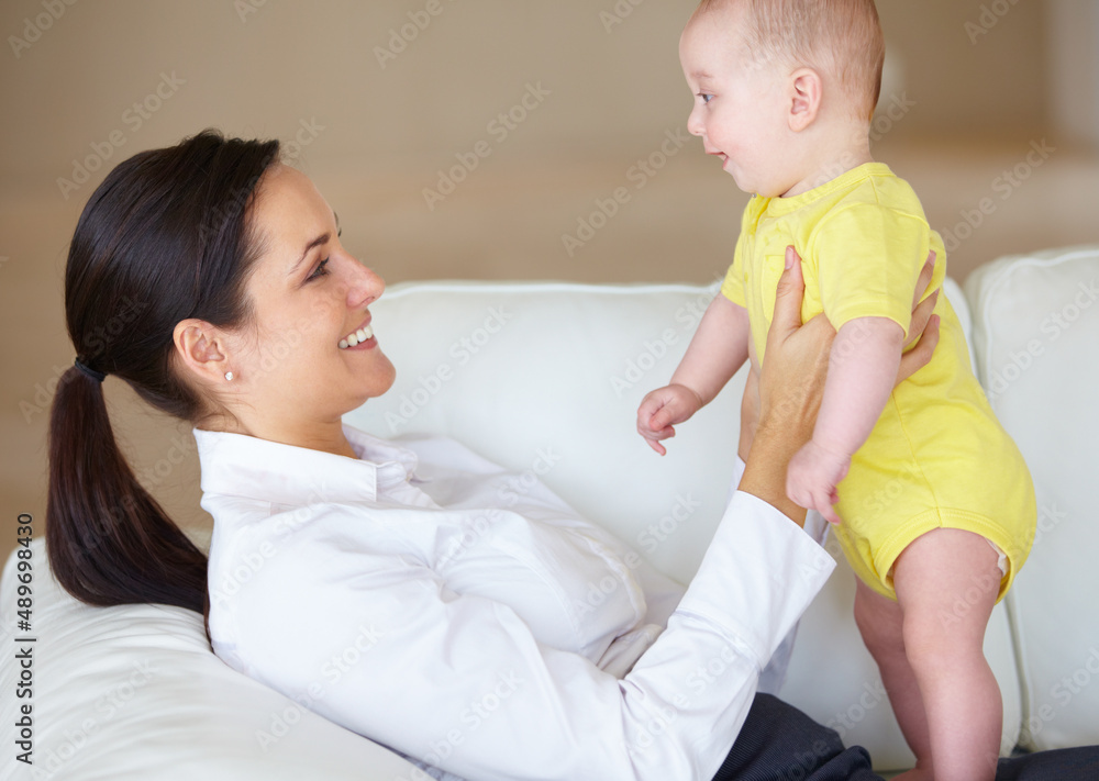 Its good to see him after a long day. Beautiful young mother playing with her baby on her couch.