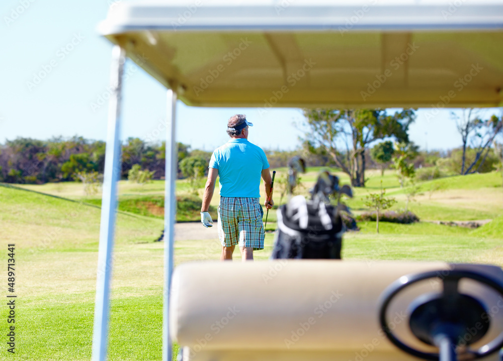 What a great day to be on the golf course.... Rear-view of a golfer walking away with a golf cart in