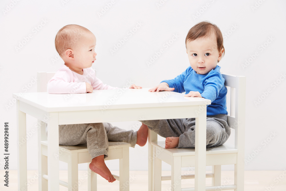 Good times with my new friend. Shot of two adorable little babies sitting together at a table.