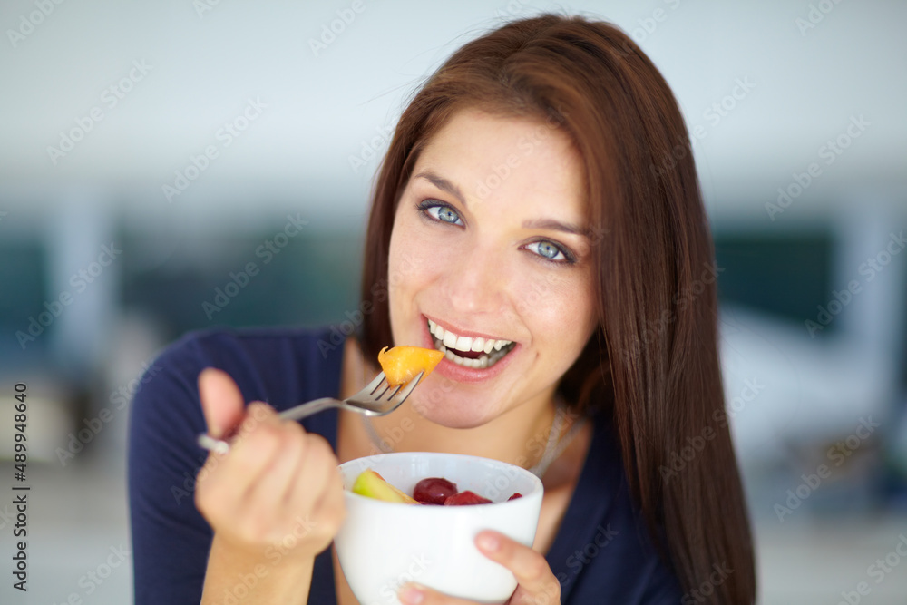 沉迷于美味健康的零食。一位微笑的年轻女子吃着健康水果沙拉的画像