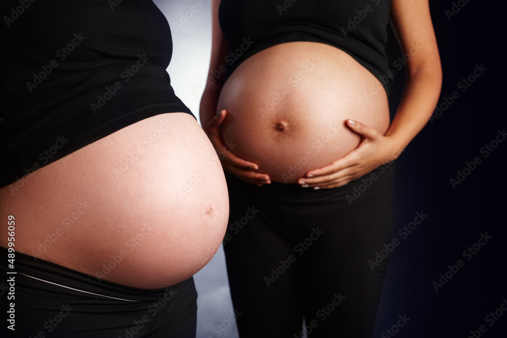 Holding new life. Close up of a ethnic womans bare pregnant stomach and a caucasian womans bare preg