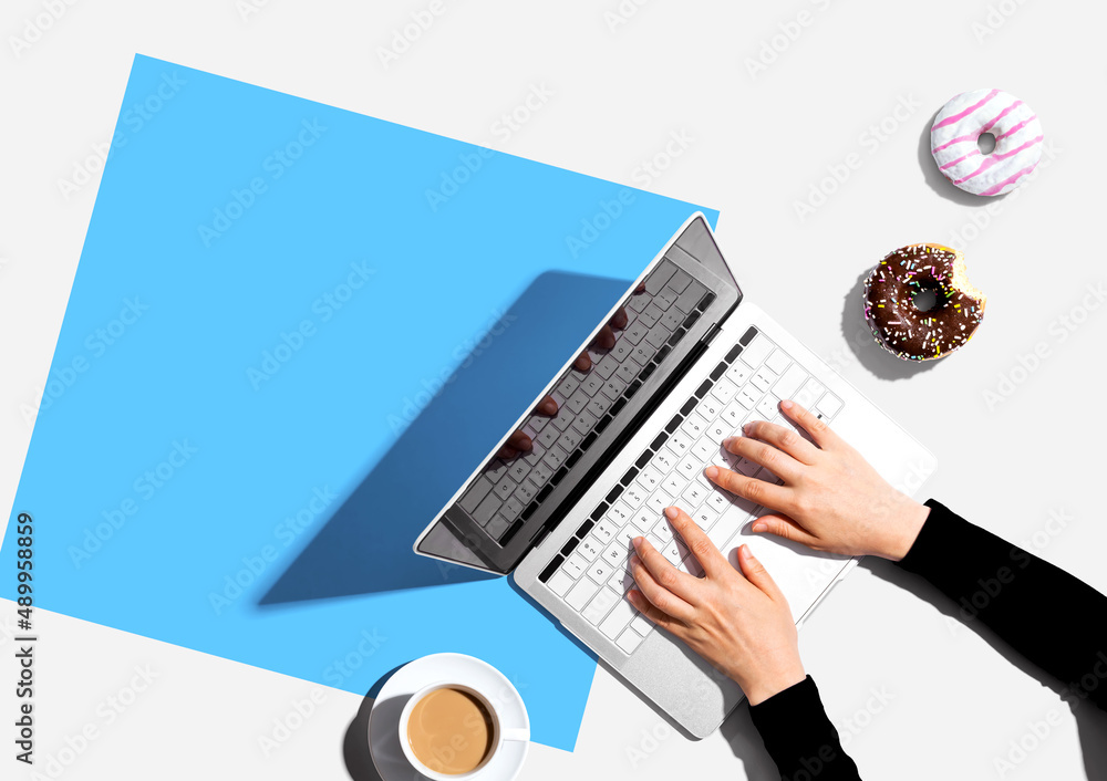 Person using a laptop computer with a donut and a cup of coffee - Flat lay