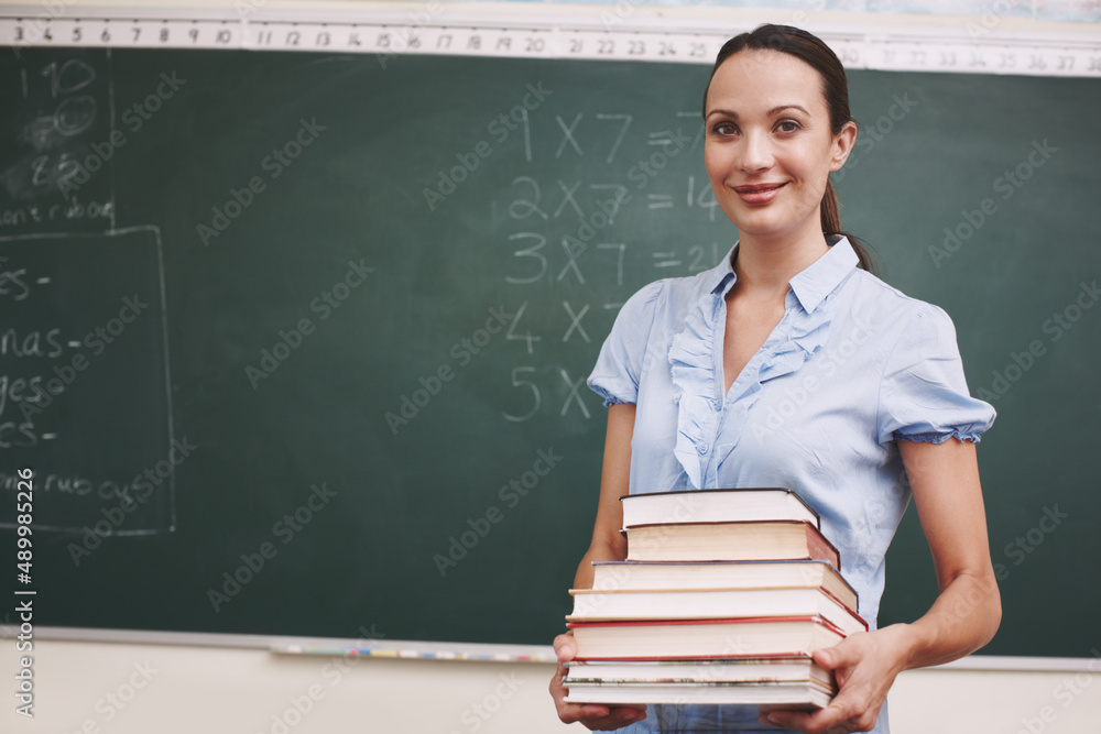 Getting ready for todays lesson. A pretty teacher holding a stack of books in her classroom.