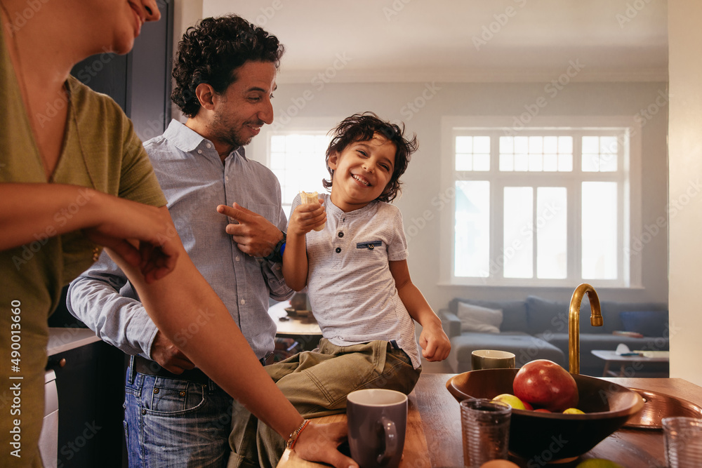 Playful little boy laughing with his parents in the kitchen