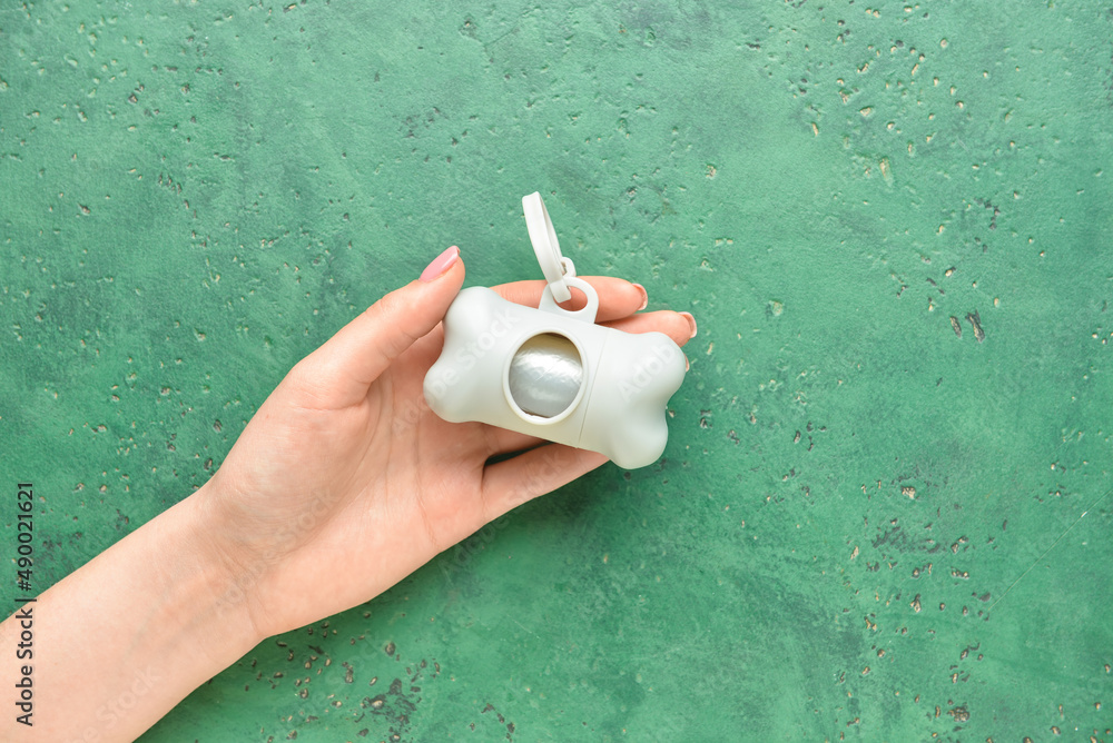 Female hand with pet waste bags on green background, closeup