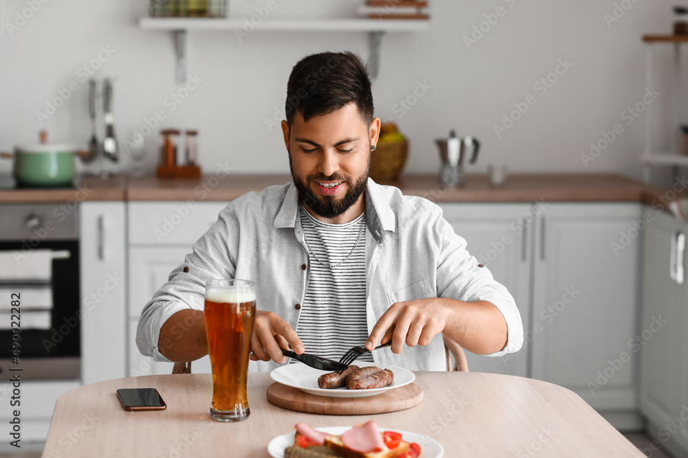 英俊的大胡子男人在厨房的桌子上吃香肠