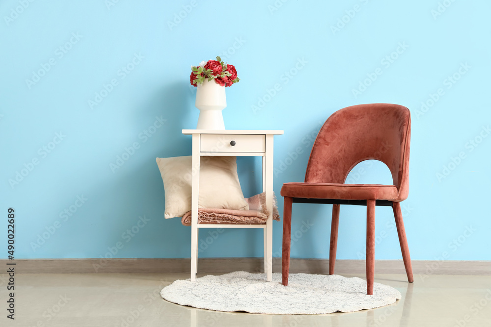 White table with flowers in vase and armchair on blue wall background