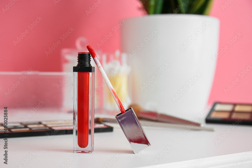 Workplace with red lip gloss and different decorative cosmetics near color wall, closeup