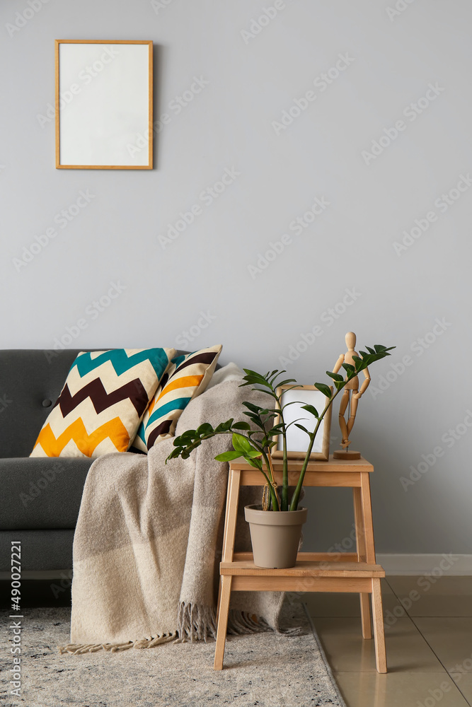 Comfortable sofa and houseplant on step ladder near light wall