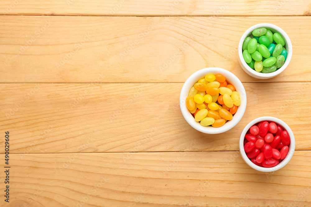 Bowls with different jelly beans on wooden background