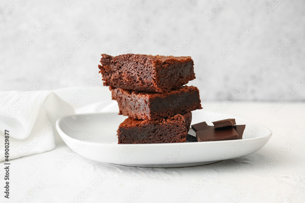 Plate with pieces of delicious chocolate brownie on light background