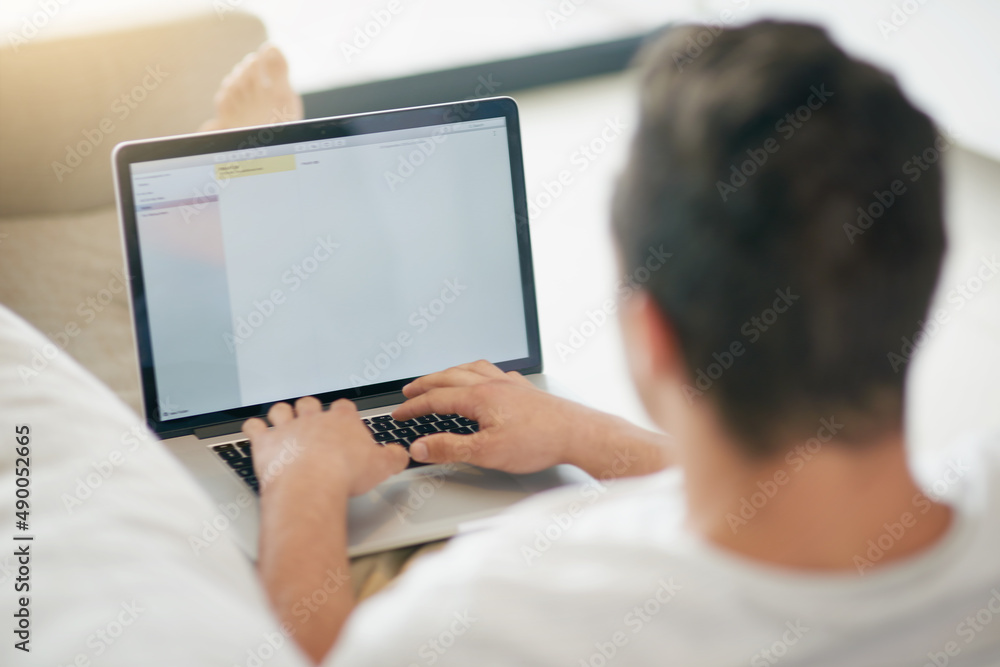 Connect and catch up with the world. Rearview shot of a relaxed young man using a laptop on the sofa