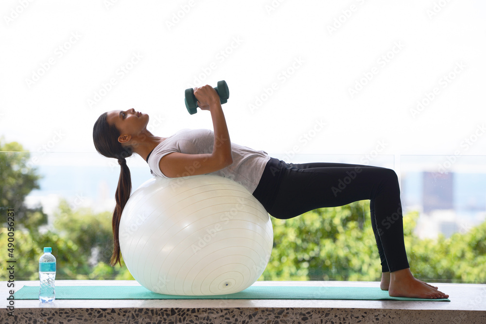 Reaching the core of zen. Shot of a young woman doing pilates by a window overlooking the city.