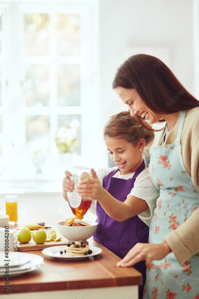 Theres no such thing as too much honey. Shot of a mother and daughter preparing food in the kitchen 