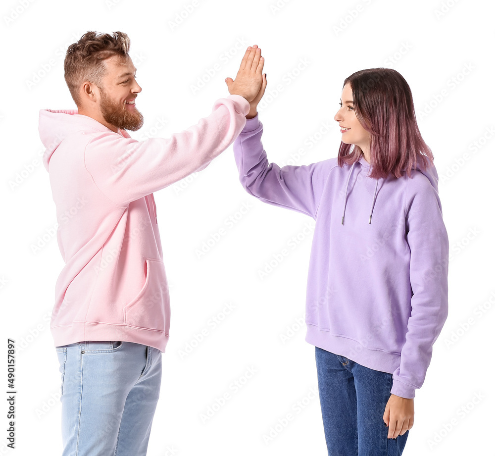 Cool young couple in hoodies giving each other high-five on white background