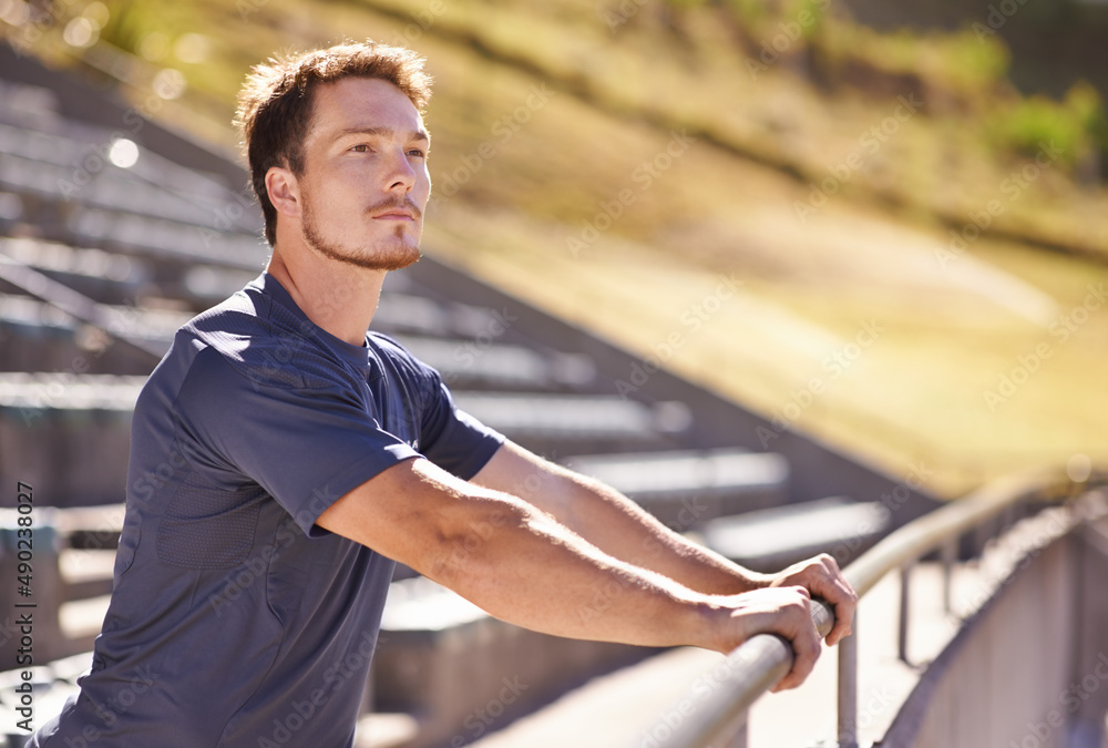 Great day to be at the track. Shot of a handsome young man stretching at an athletics arena.