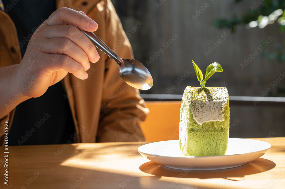 女人在吃之前用勺子切一块抹茶绿茶蛋糕卷。抹茶蛋糕是用f做的。