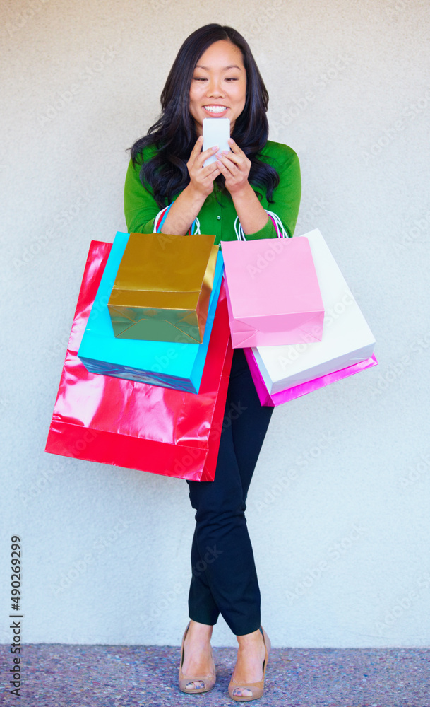 Stopping for an sms while shopping. A young asian woman sending a text message while shopping.