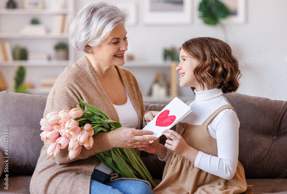 Cheerful little girl giving flowers  and handmade postcard to grandmother