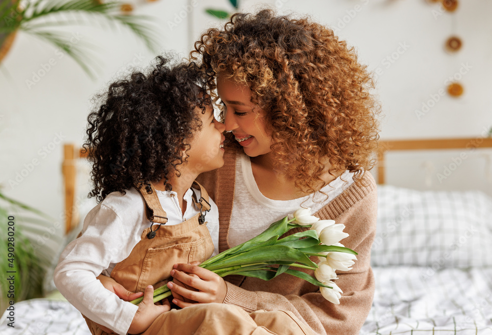 Grateful ethnic mother with bouquet hugging son