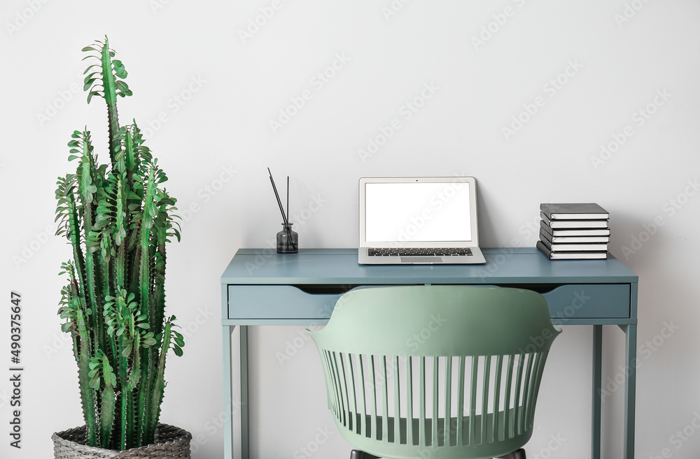 Modern workplace with laptop and big cactus near light wall