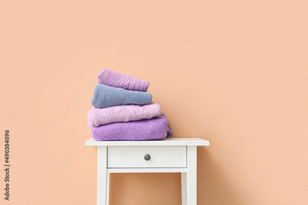 Knitted sweaters on table near color wall