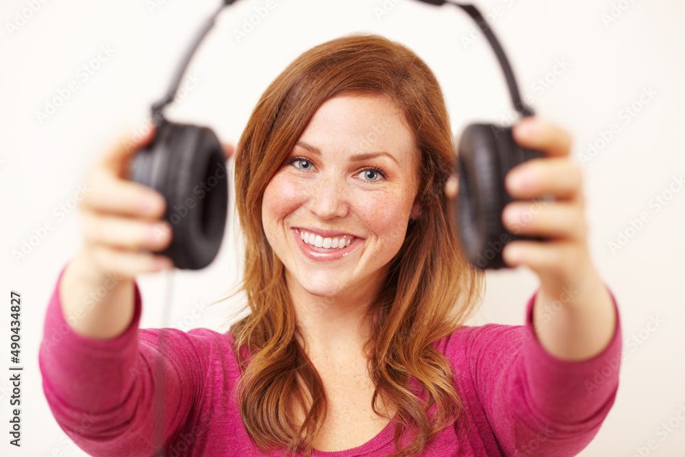 Hear, have a listen to this. Portrait of an attractive young woman offering you a pair of headphones