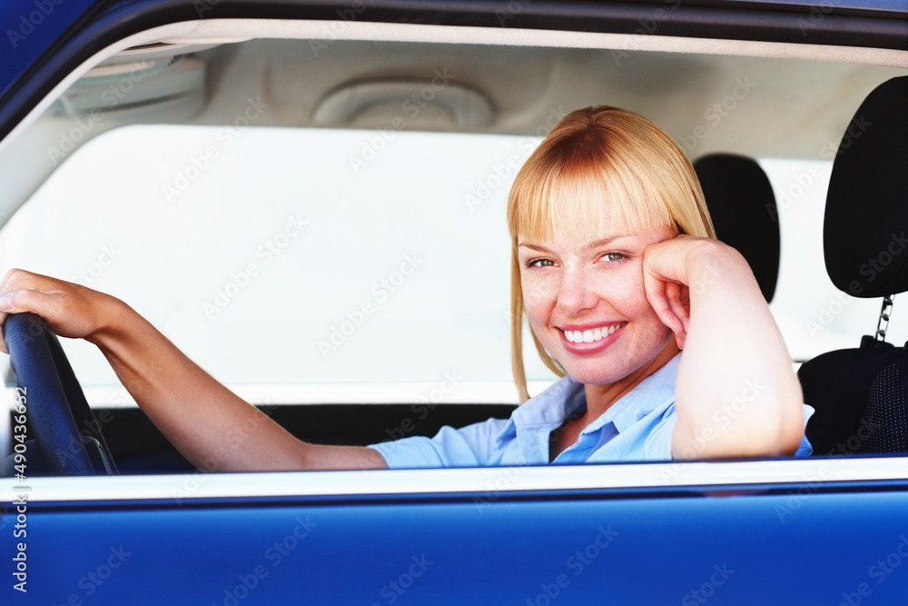 Pretty woman smiling from the drivers seat of a car. Smiling blond woman in a car sitting at the dri