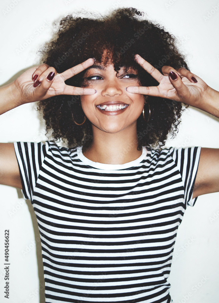 Fun on fleek. Studio shot of a playful young woman showing the peace sign against a gray background.