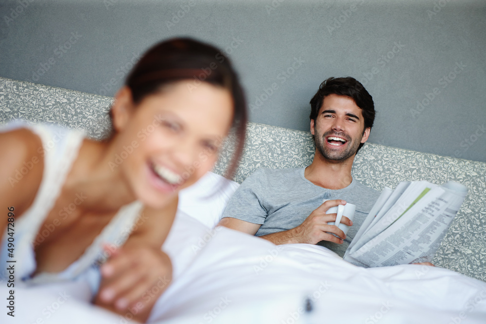 Relaxed and happy. Shot of a man in bed smiling at his girlfriend with a newspaper and mug in his ha