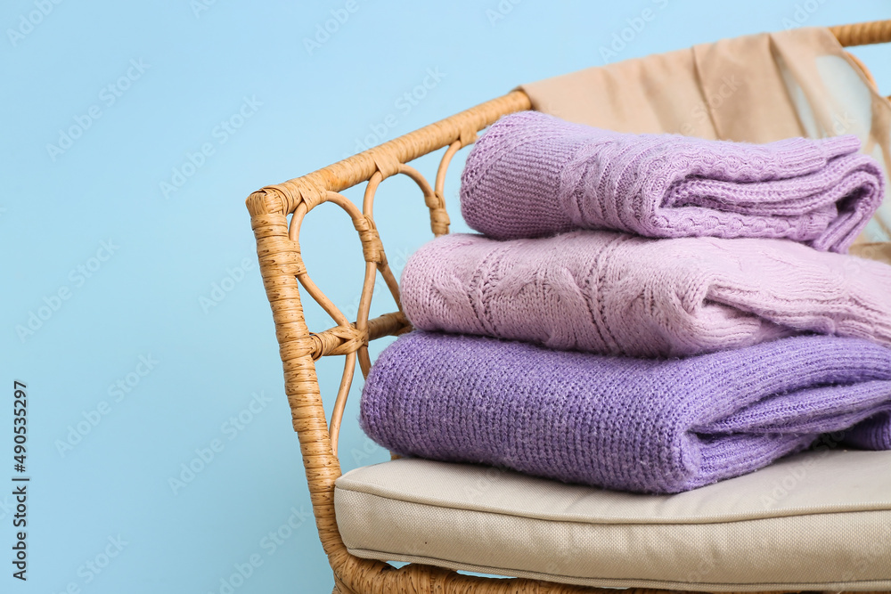 Wicker armchair with stack of lilac sweaters near blue wall