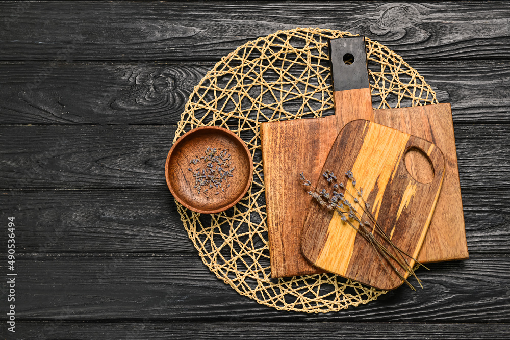 Wooden cutting boards, bowl and lavender flowers on black wooden background