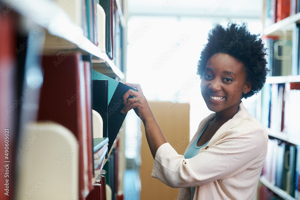 Studying for my final exam. A young woman selecting some books in the library.