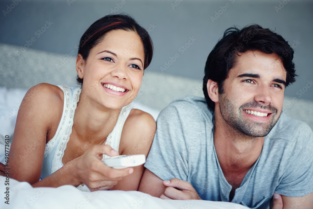 Bonding over our favourite television programmes. Shot of a happy couple lying on their bed watching