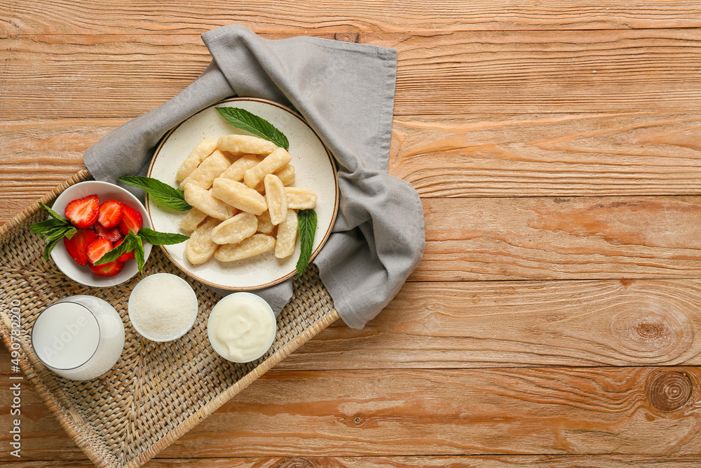 Tray with tasty lazy dumplings, strawberry, sugar, sour cream and glass of milk on wooden background