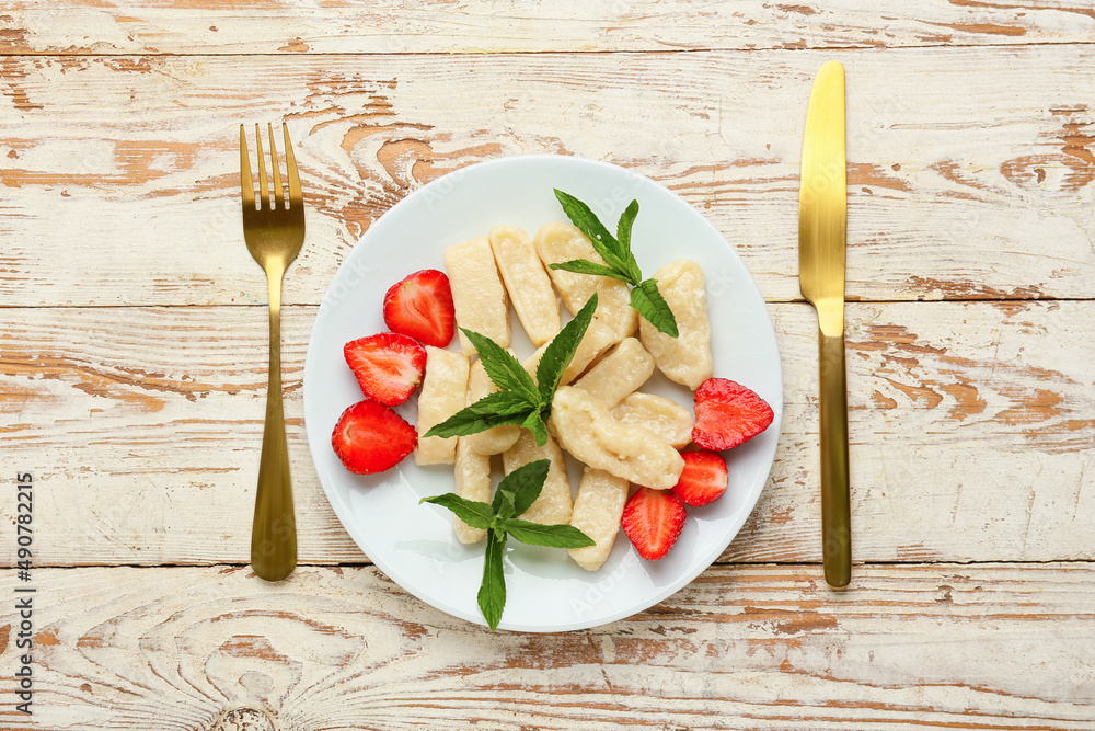 Plate with tasty lazy dumplings, strawberry, mint and cutlery on light wooden background