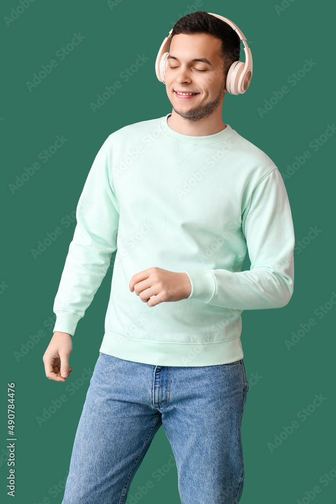 Young man in wireless headphones listening to music on green background