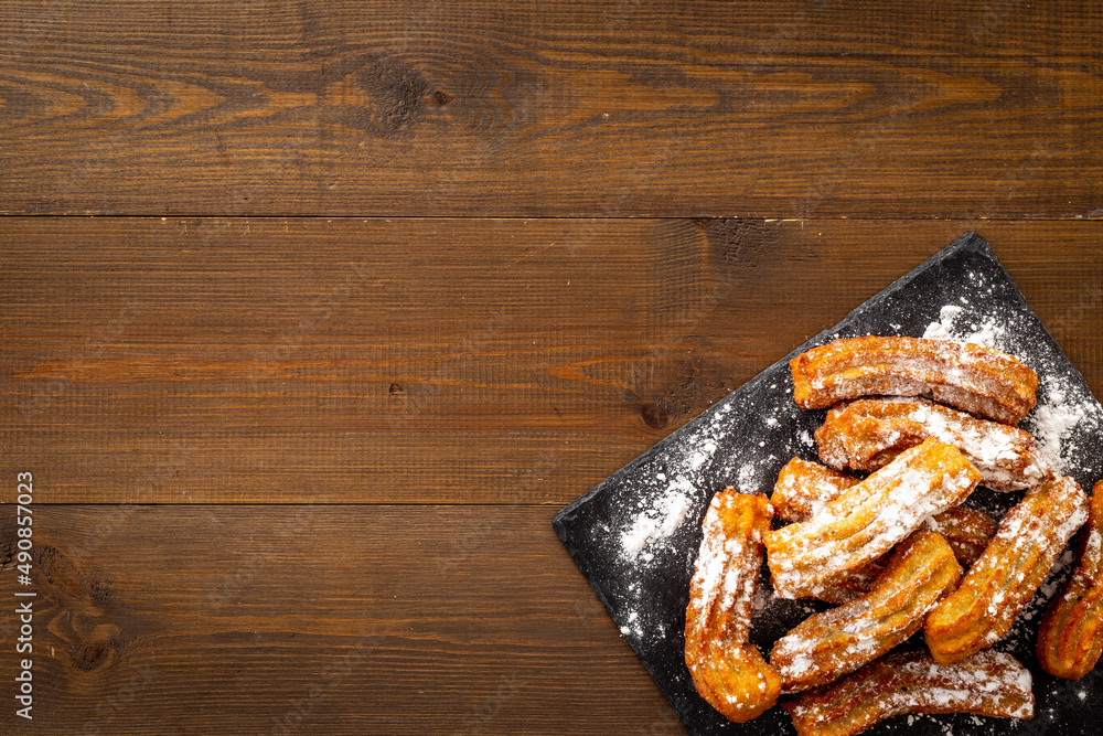 黑盘子里有糖粉的Churros。油腻的快餐糖果