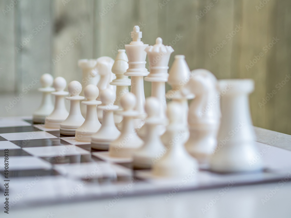 White chess pieces are in the correct order on the chess board. Staunton chess set. Close-up.