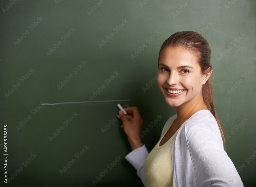 Shaping the future generation. A beautiful young teacher writing on a blackboard while smiling at th