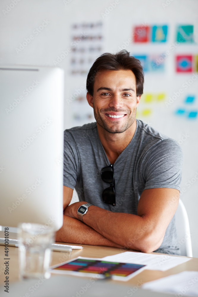 Job satisfaction. A handsome young man sitting and smiling in front of his computer.