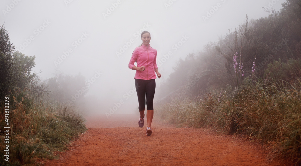 The only way she likes to run. Shot of a woman running on a trail on a misty morning.