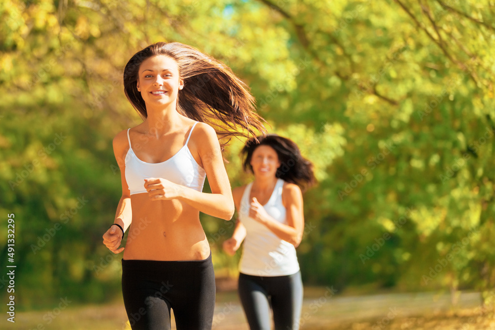 Friendly compteition. Shot of two young women jogging together in a park in autumn.