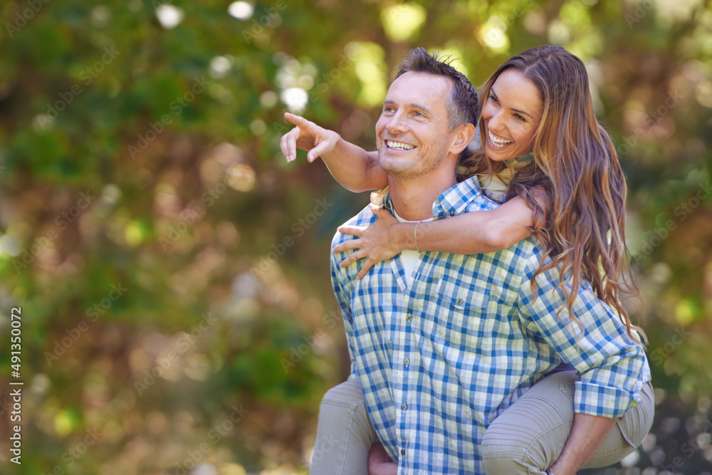 Look over there. A handsome man giving his wife a piggyback outdoors.